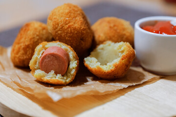 Potato crockets with filling sausages on wooden board with ketchup sauce. Side view. Close up.