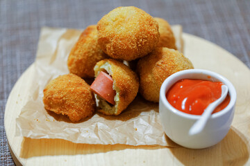 Fried crocket from potato with filling sausages on wooden board with ketchup sauce. Side view. Close up.