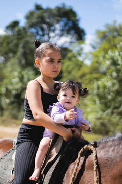 A baby smiling with her sister on a horse