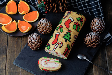 Christmas desserts: roll with traditional Christmas patterns, chocolate cakes shaped tree cones and orange jelly on black board, wooden table, black background. View above.
