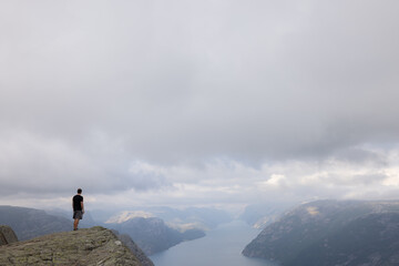 Fantasy Adventure Composite with a Man on top of a Mountain Cliff with Dramatic Landscape in Background during Sunset or Sunrise. Landscape from Preikestolen, Norway. Way to success.