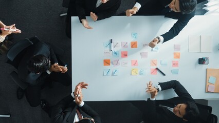 Top down aerial view of business group sharing and brainstorming idea by using sticky notes at meeting room. Investor writing marketing strategy on board while receive note from manager. Directorate.