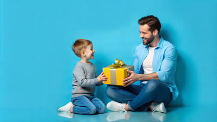 happy father and son with gift box sitting on floor on blue background