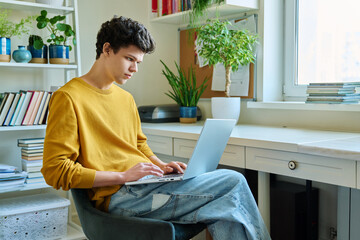 Young male college student using laptop, sitting at home