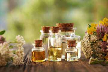 Bottles of aromatherapy essential oil with colorful summer flowers on a table