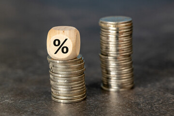 Smaller and larger stack of coins, Percent symbol on wooden cube placed on top. Financial concept