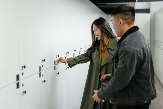 Man with suitcase looking at smiling girlfriend opening storage locker