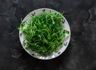 Pea sprouts in a bowl on a dark background, top view