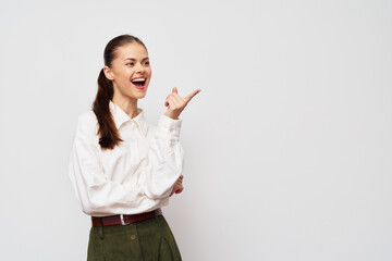 Happy young woman in a white shirt pointing excitedly, smiling and engaging with a light gray background, conveying positive energy and enthusiasm