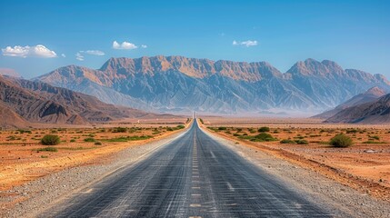 A winding road stretches through a vast desert landscape, framed by majestic mountains under a clear blue sky