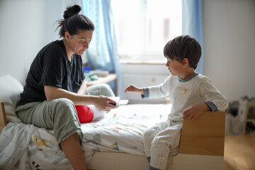 Obraz premium Mother and son sharing a moment in the child's bedroom, with the mother handing something to the child. The scene captures a warm and nurturing interaction in a cozy home environment.