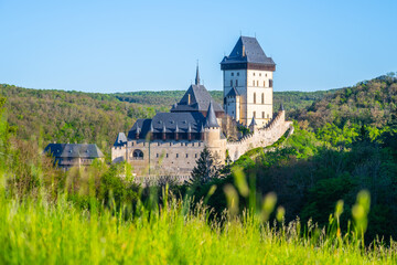 The majestic Karlstejn Castle stands proud against a backdrop of lush greenery as the morning sun rays enhance its architecture. A peaceful scene unfolds in this historic location of Czechia.