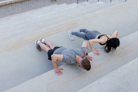 Fitness woman doing push-ups with personal trainer on stairs