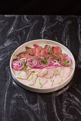 The Elegant Plating of Thinly Sliced Beef Accompanied by Tender Onions and Garnishes