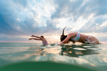 Two girls diving into the calm water at sunset