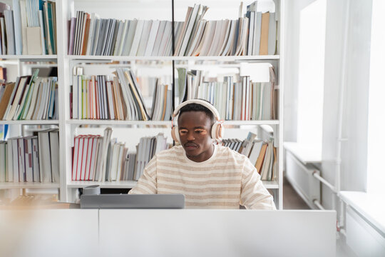 Student wearing headphones studying in bright library