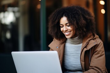 Fototapeta premium Smiling woman with curly hair using laptop outdoors on a cozy day