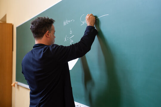 Teacher writes math equations on classroom chalkboard