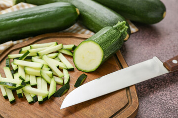 Fresh green zucchini and board with slices on purple background