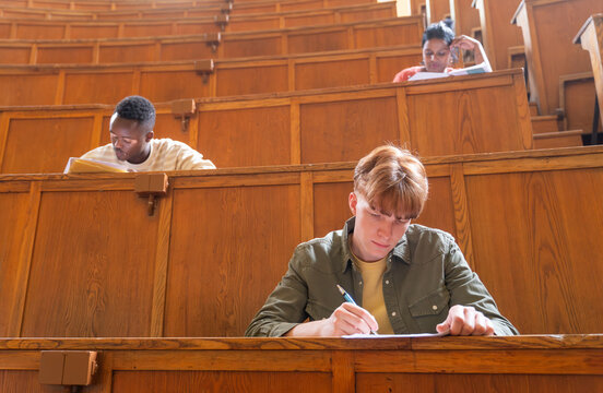 Students writing notes in a wooden lecture hall