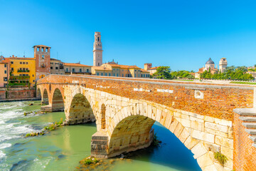 The ancient Ponte Pietra stone arch bridge crossing the Adige River, with the bell tower of the Verona Cathedral Duomo rising above the medieval old town, Verona, Italy.	