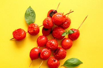 Skewers with tasty grilled tomatoes and basil on yellow background