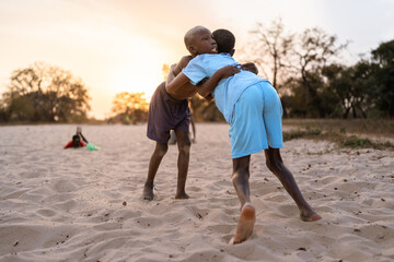 Two young boys wrestling in the sand at sunset in senegal