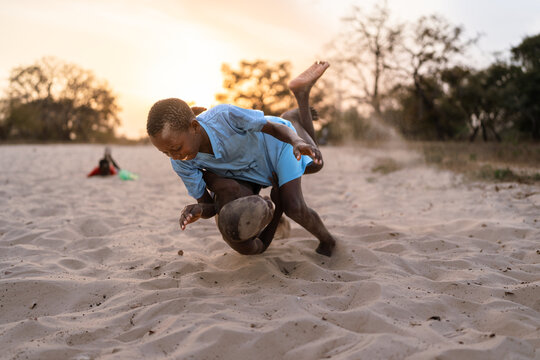 Two boys wrestling in sand practicing senegalese wrestling at sunset