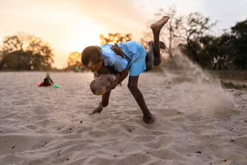 Two african kids playing wrestling in the sand at sunset