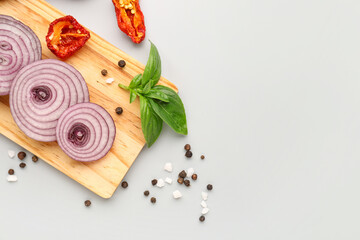 Board with fresh onion slices and spices on light background