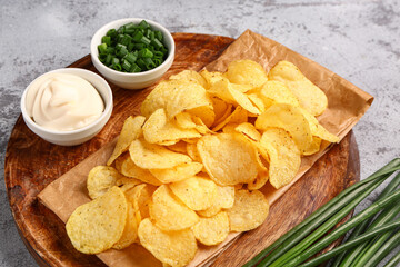 Bowls of tasty sour cream with sliced green onion and potato chips on grey background
