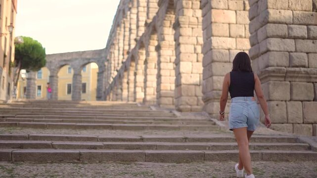 Aqueduct of Segovia visited by girl travelling to Spain walking arround this artichetectural structure which is considered as a world heritage.