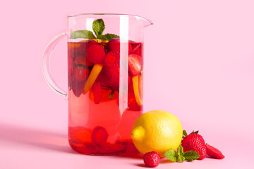 Jug of infused water with strawberry and lemon on pink background
