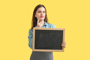 Thoughtful female teacher with chalkboard on yellow background