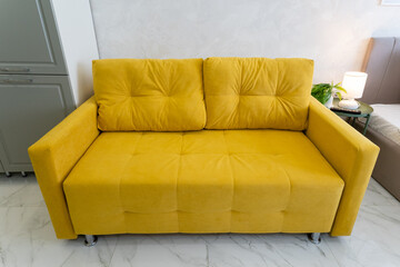 A bright yellow couch is positioned in a cozy living room beside a bed