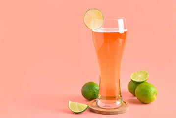 Glass of cold beer with lime on pink background