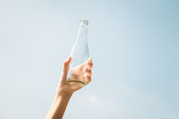Recyclable glass bottle held in hand up on sky background. Hand holding plastic waste for recycle...