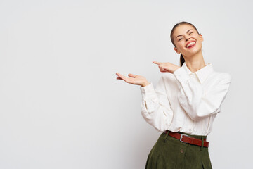 Smiling woman in a white shirt showing something with her hands, standing against a plain light...