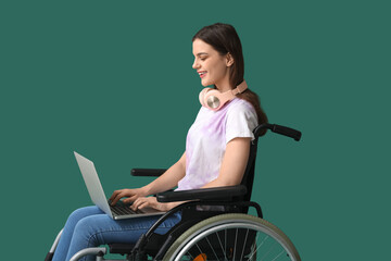 Young woman in wheelchair using laptop on green background