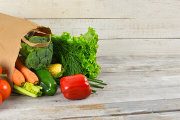 Paper bag full of fresh vegetables on white wooden table near wall