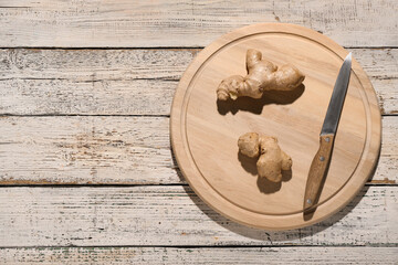 New cutting board with knife and ginger on light wooden background