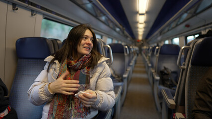 Woman Engaging In Conversation While Sitting On A Train, Dressed Warmly In A White Jacket And Colorful Scarf, Expressing Emotions, Interaction During Travel, Spacious Interior Of The Train