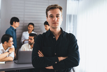 Obraz premium Confidence and happy smiling businessman portrait with background of his colleague and business team working in office. Office worker teamwork and positive workplace concept. Prudent