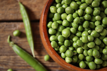 Bowl with fresh green peas on wooden background