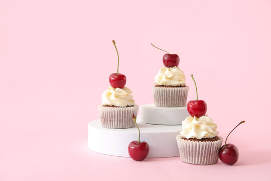 Decorative stand with tasty cherry cupcakes on pink background