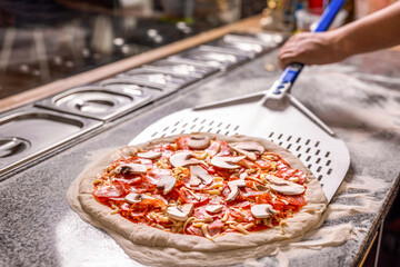 The chef prepares pizza with a shovel in his hands. Raw pizza ready to bake. Cook in the kitchen with a shovel in his hands. Man prepares pizza. Cook hand makes a pizza © Yevhen