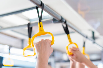Passengers holding yellow hand grips on a public transport vehicle during a morning commute