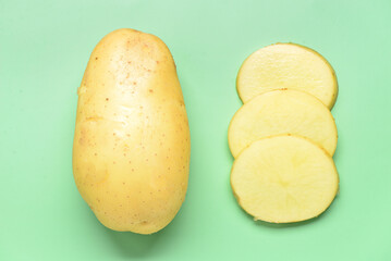Whole and cut potatoes on green background