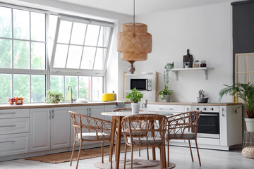 Interior of light kitchen with white counters, dining table and big window