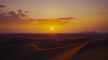   The sun is setting over a desert with sand dunes in the foreground and mountains in the distance